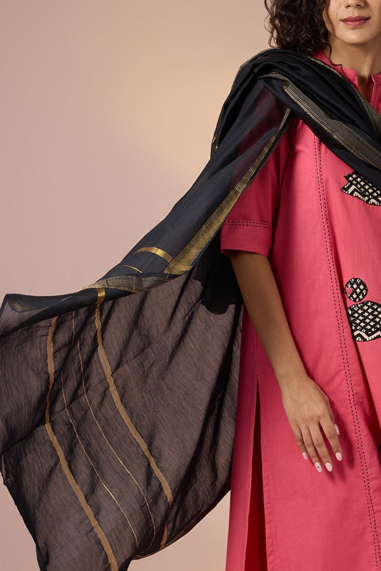 Woman wearing a pink traditional outfit with a black dupatta against a beige background